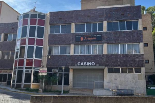 Fachada de un edificio urbano con letrero de “Casino”, varias plantas, grandes ventanales y una entrada cerrada con persiana metálica.