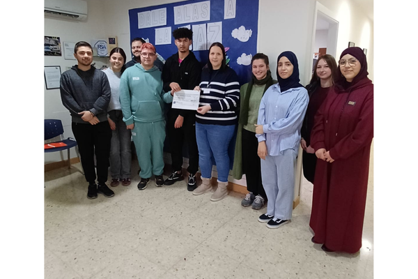 Grupo de personas posando en un aula; dos de ellas sostienen un documento frente a un mural azul.
