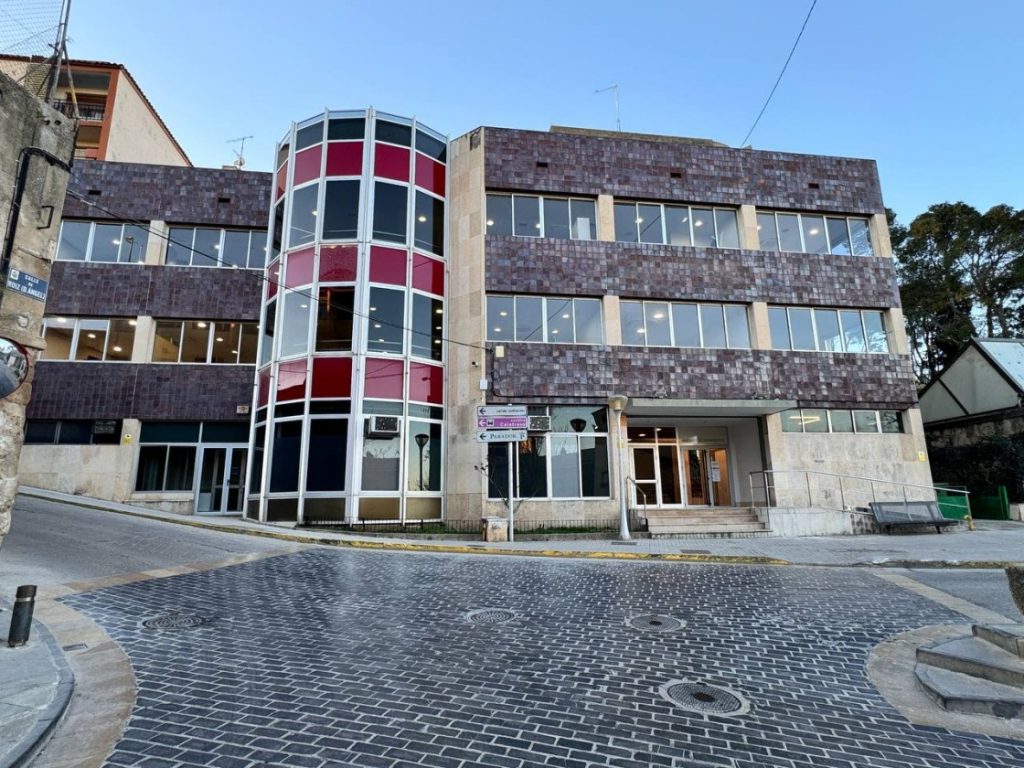 Vista exterior del Ayuntamiento de Alcañiz, un edificio moderno con amplios ventanales y una torre central acristalada.